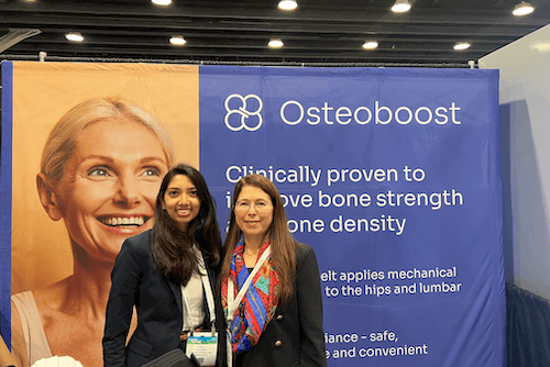 Two women stand in front of a booth at ASBMR 2023